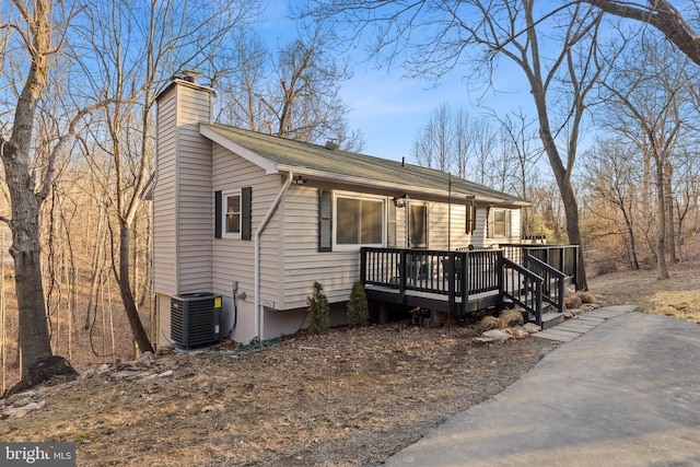 view of front of property featuring driveway, a chimney, a wooden deck, and central AC unit