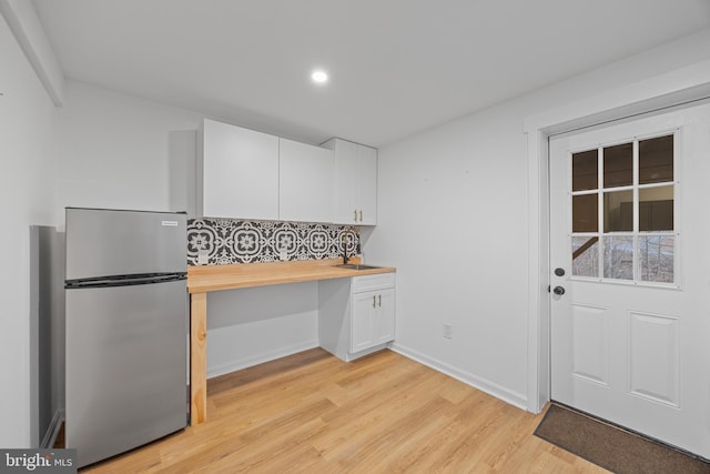 kitchen featuring butcher block counters, white cabinetry, light wood-type flooring, freestanding refrigerator, and built in desk