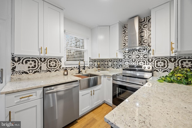 kitchen with white cabinets, wall chimney range hood, stainless steel appliances, and a sink