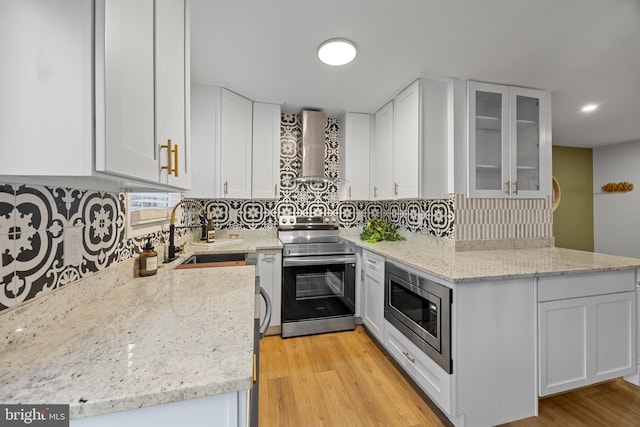 kitchen with stainless steel appliances, white cabinets, a sink, light stone countertops, and wall chimney exhaust hood