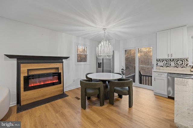 dining space featuring a notable chandelier, light wood-style flooring, a wealth of natural light, and a glass covered fireplace