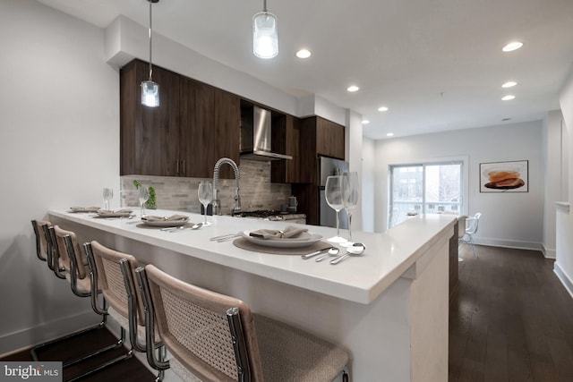 kitchen with a peninsula, light countertops, freestanding refrigerator, wall chimney exhaust hood, and modern cabinets