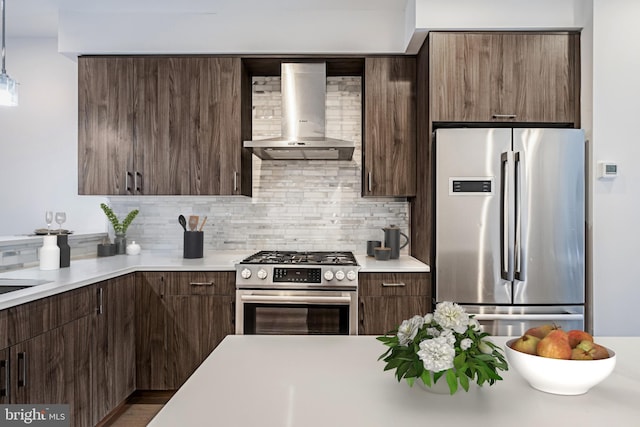 kitchen with stainless steel appliances, dark brown cabinets, light countertops, backsplash, and wall chimney exhaust hood