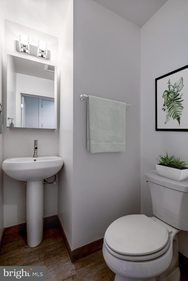 half bath featuring a sink, wood finished floors, toilet, and baseboards