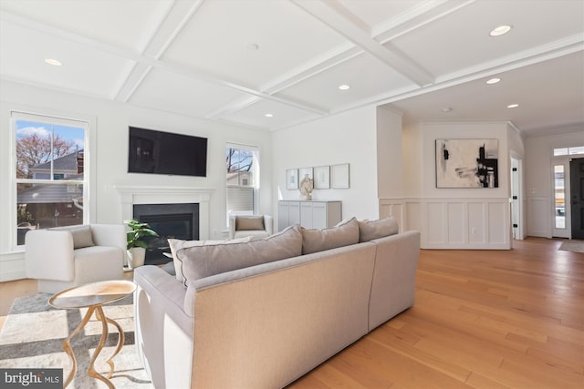 living room featuring a wealth of natural light, light wood-type flooring, coffered ceiling, and a glass covered fireplace