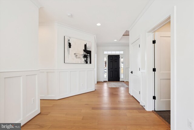 corridor with a wainscoted wall, recessed lighting, light wood-style floors, crown molding, and a decorative wall