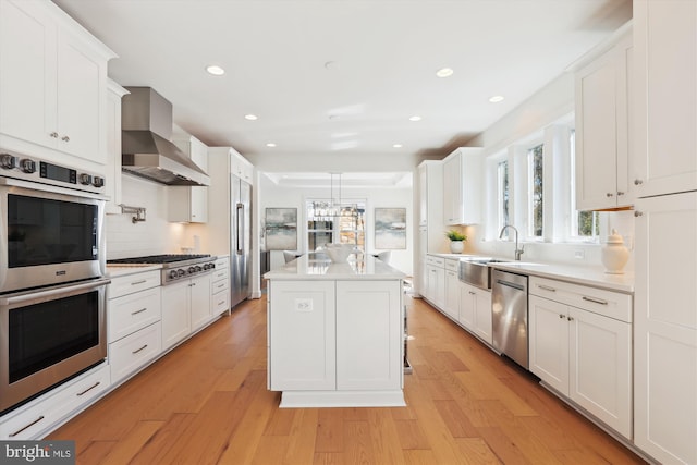 kitchen featuring a sink, a kitchen island, appliances with stainless steel finishes, wall chimney exhaust hood, and white cabinets