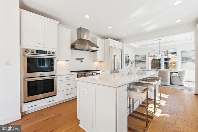 kitchen featuring a breakfast bar, wall chimney range hood, light wood-type flooring, and stainless steel appliances