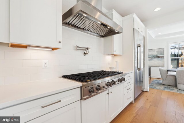 kitchen with light wood-type flooring, appliances with stainless steel finishes, wall chimney exhaust hood, and white cabinets