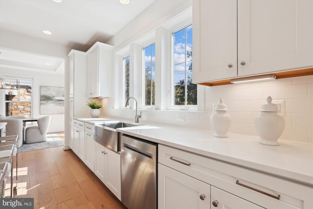 kitchen featuring light wood-style flooring, decorative backsplash, light countertops, white cabinets, and stainless steel dishwasher