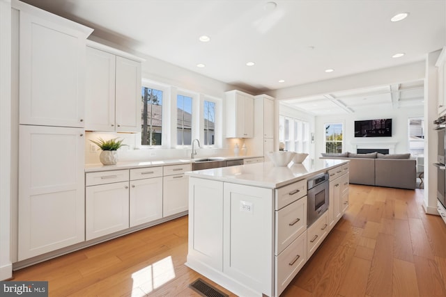 kitchen featuring a sink, visible vents, light wood-style floors, and white cabinetry