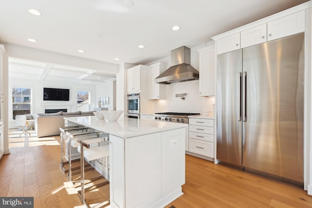 kitchen featuring white cabinetry, wall chimney range hood, light wood-style floors, and appliances with stainless steel finishes