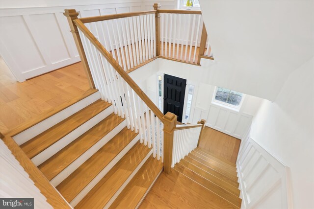 stairs featuring a decorative wall, wood finished floors, a high ceiling, and wainscoting