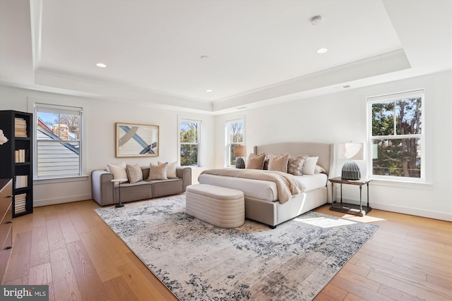 bedroom featuring light wood finished floors, a raised ceiling, and baseboards