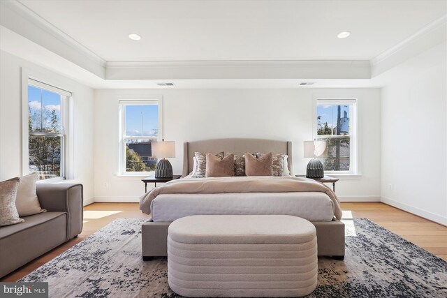 bedroom with a raised ceiling, crown molding, baseboards, and light wood finished floors