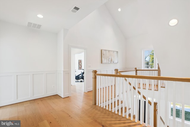 hall with light wood-type flooring, visible vents, an upstairs landing, recessed lighting, and wainscoting