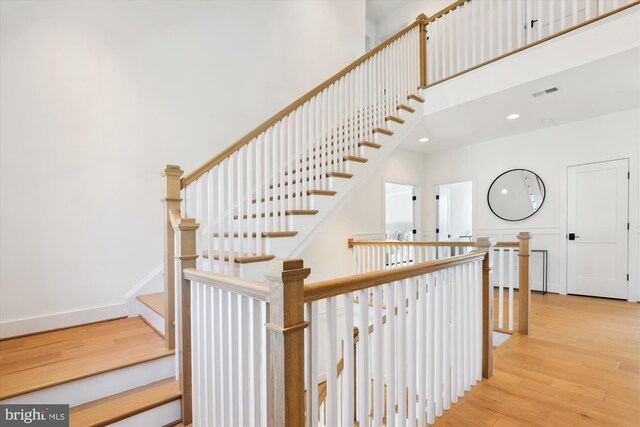 stairs with wood finished floors, visible vents, baseboards, recessed lighting, and a towering ceiling