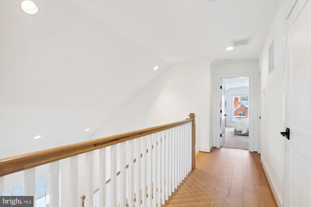 hallway featuring visible vents, an upstairs landing, lofted ceiling, light wood-style flooring, and baseboards