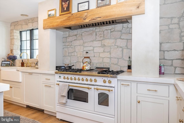 kitchen featuring light wood finished floors, white cabinets, ventilation hood, light countertops, and double oven range