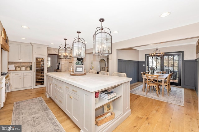 kitchen featuring a wainscoted wall, a notable chandelier, light wood-style floors, white cabinetry, and a kitchen island