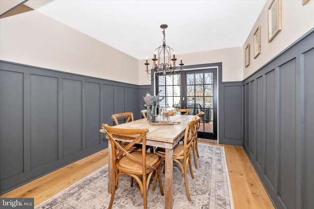 dining area with wainscoting, light wood-style flooring, and an inviting chandelier