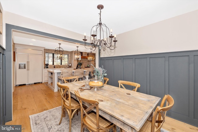 dining area with a wainscoted wall, light wood-style floors, a decorative wall, and an inviting chandelier