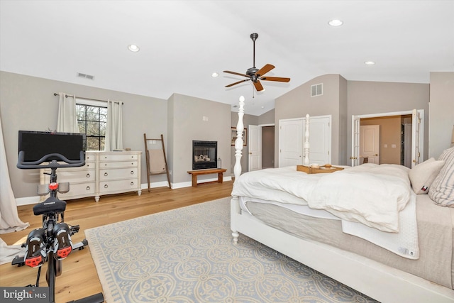 bedroom featuring vaulted ceiling, a glass covered fireplace, wood finished floors, and visible vents