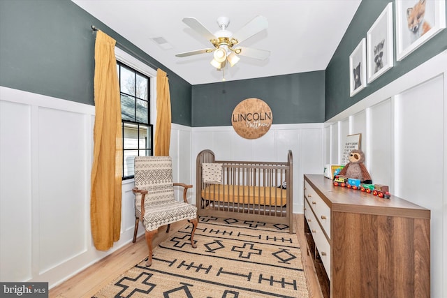 bedroom with light wood-style floors, a wainscoted wall, a decorative wall, and visible vents