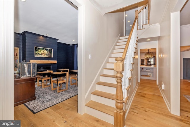 stairs with a notable chandelier, recessed lighting, wood finished floors, baseboards, and crown molding