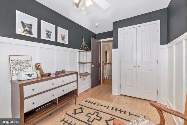 bedroom featuring light wood-type flooring, a closet, wainscoting, and a decorative wall