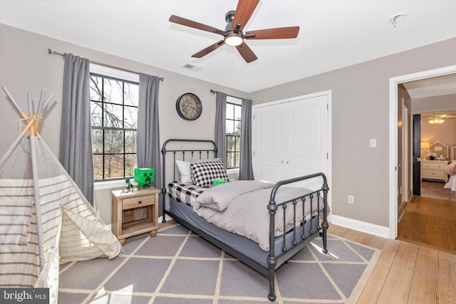 bedroom with baseboards, visible vents, wood-type flooring, ceiling fan, and a closet