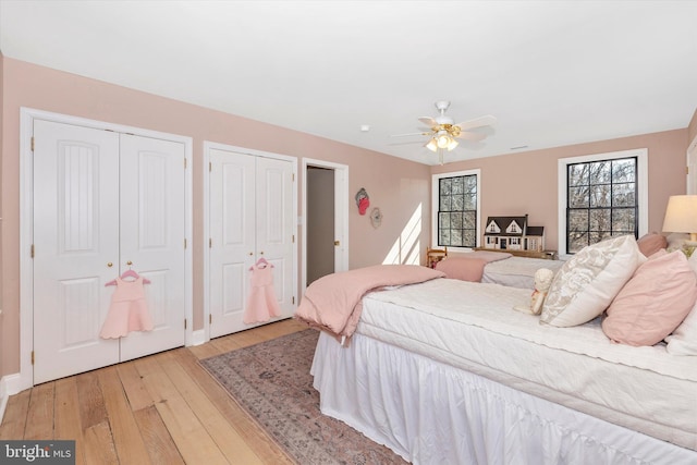 bedroom with light wood-type flooring, two closets, and a ceiling fan