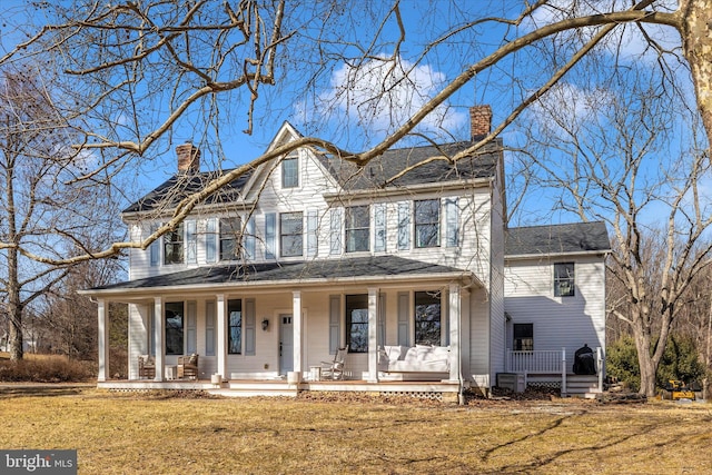 shingle-style home with a front yard, covered porch, and a chimney