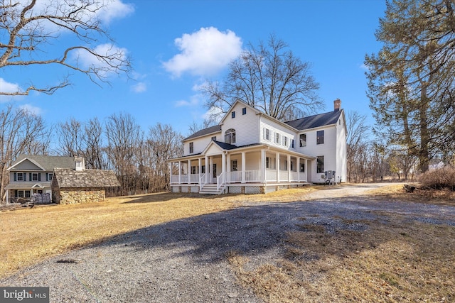 view of front of house with driveway, covered porch, a chimney, and a front yard