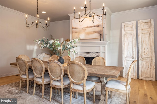 dining space featuring light wood finished floors, baseboards, a tiled fireplace, ornamental molding, and an inviting chandelier