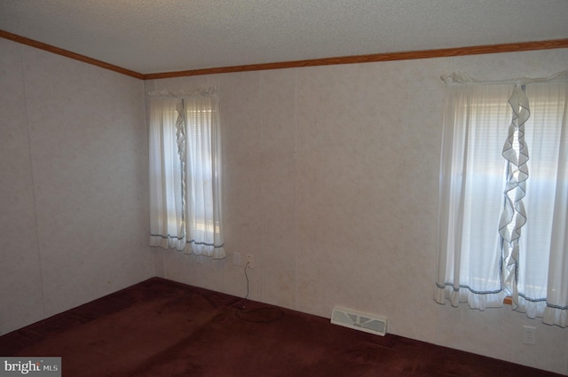 empty room featuring a textured ceiling, carpet, visible vents, and crown molding