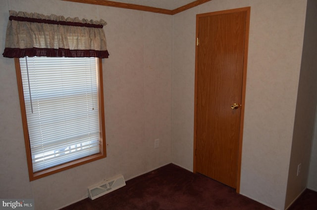 spare room with visible vents, dark colored carpet, and crown molding