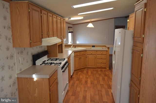 kitchen with light countertops, a sink, white appliances, under cabinet range hood, and wallpapered walls