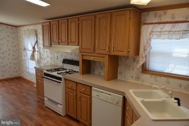 kitchen featuring light countertops, a sink, white appliances, under cabinet range hood, and wallpapered walls