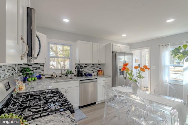 kitchen with light wood finished floors, stainless steel appliances, white cabinetry, a sink, and light stone countertops