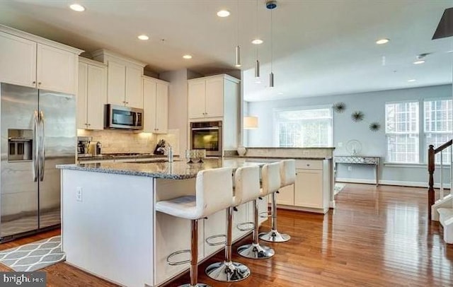 kitchen with appliances with stainless steel finishes, stone countertops, decorative backsplash, and wood finished floors