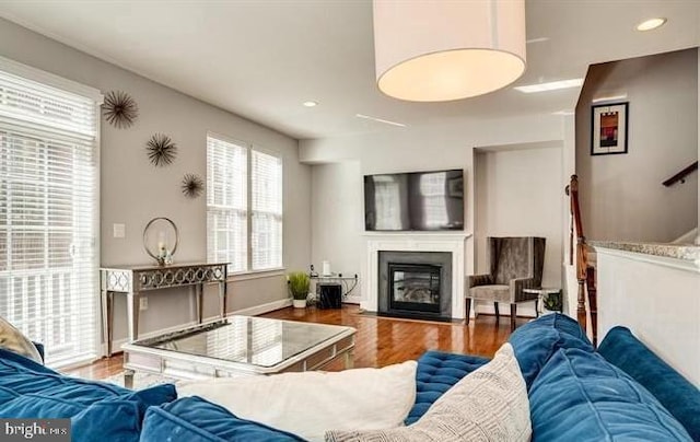 living room featuring a fireplace with flush hearth, baseboards, wood finished floors, and recessed lighting