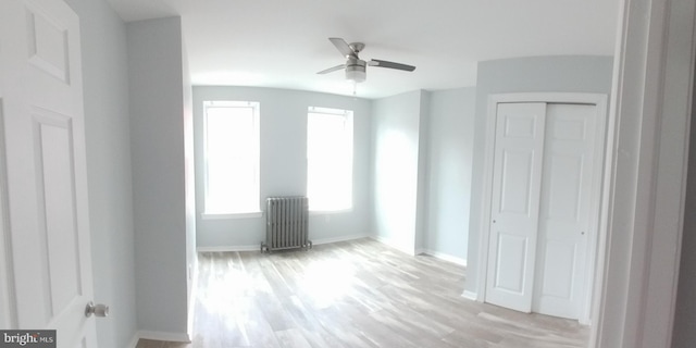 unfurnished bedroom with light wood-style floors, a closet, baseboards, and radiator heating unit