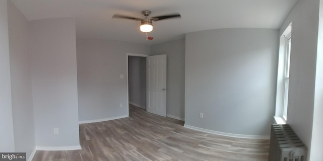 spare room featuring ceiling fan, radiator heating unit, wood finished floors, and baseboards