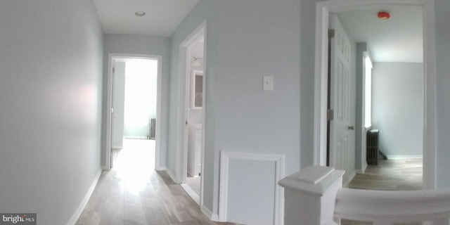 hallway with baseboards, wood finished floors, and radiator