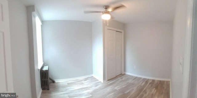 unfurnished bedroom with light wood finished floors, radiator heating unit, a closet, and baseboards