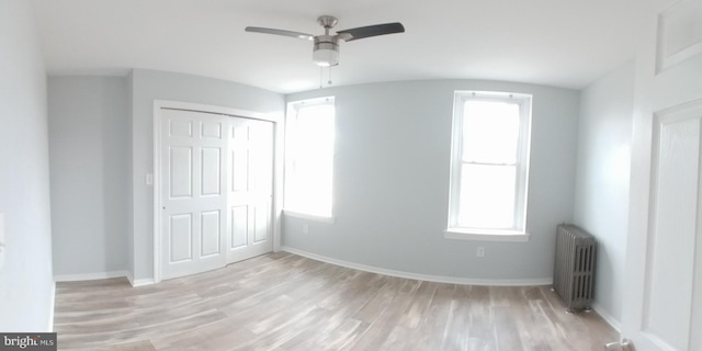 unfurnished bedroom featuring a ceiling fan, baseboards, a closet, light wood finished floors, and radiator heating unit