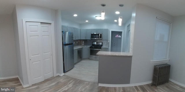 kitchen featuring decorative light fixtures, light countertops, decorative backsplash, radiator heating unit, and appliances with stainless steel finishes