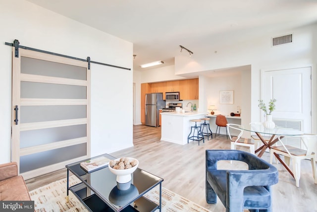 living area with a barn door, visible vents, and light wood-style floors