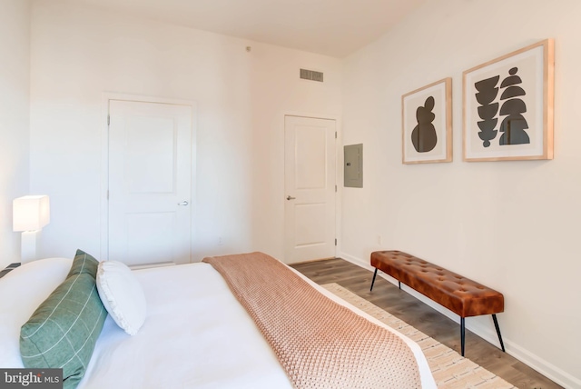 bedroom featuring baseboards, electric panel, visible vents, and wood finished floors